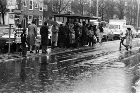 Afgelopen_dagen_heeft_het_bijna_aan_een_stuk_door_geregend_mensen_bij_een_bushalte,_Bestanddeelnr_931-3659
