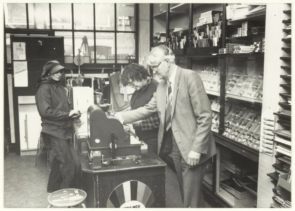 Adrianus M. Pompe in zijn winkel in kunstschildersartikelen aan de Gierstraat 29. Op de achtergrond helpt Margreet Glasbergen een klant. NL-HlmNHA 54015541