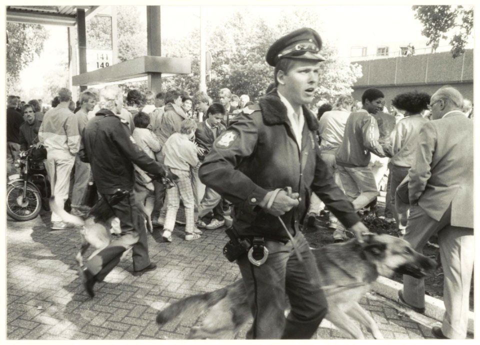 Ajax supporters en politie hondenbegeleider tijdens oproer bij het benzinestation aan de Planetenlaan, nabij de Rijksstraatweg, ziende naar het noordoosten. NL-HlmNHA 54015266