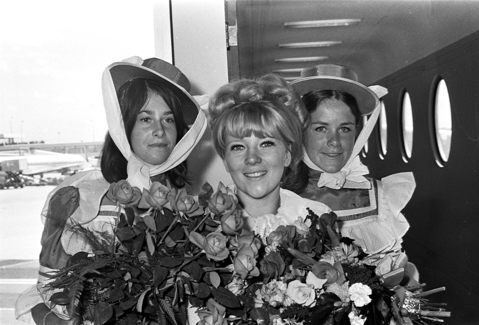 Aankomst filmster Julia Foster op Schiphol omringd door meisjes in costuums anno, Bestanddeelnr 921-4849