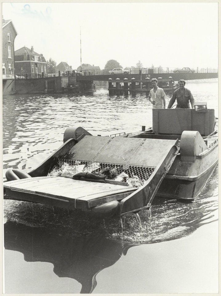 Alle rotzooi in het water van het Spaarne wordt door Henny van der Han met zijn reinigingsvlet naar boven gehaald. Op de achtergrond de Catharijnebrug., NL-HlmNHA 54012342