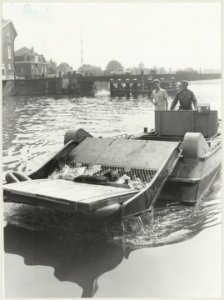 Alle rotzooi in het water van het Spaarne wordt door Henny van der Han met zijn reinigingsvlet naar boven gehaald. Op de achtergrond de Catharijnebrug., NL-HlmNHA 54012342