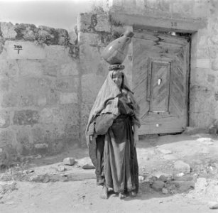 Arabische vrouw met waterkruik op het hoofd bij een gesloten poort, Bestanddeelnr 255-1426