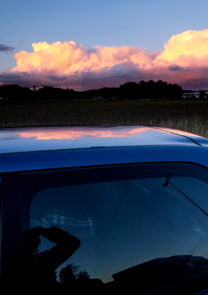 Bank of pink clouds reflected in the roof of a blue car 2