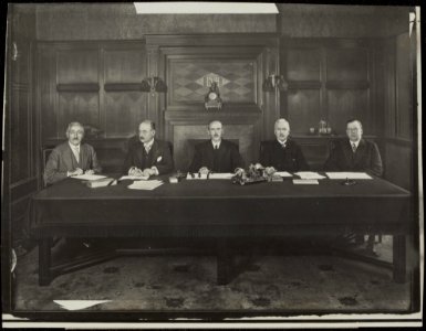 Bestuur en directie achter tafel in kamer met lambrisering v.l.n.r B.B.M. Rupe, Bestanddeelnr 839 22