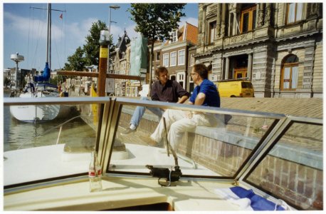 Bert Sliggers (l) in gesprek met een heer gezien vanaf een boot langs de kade bij het Teylers museum. NL-HlmNHA 54036098