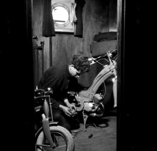 Bemanningslid Otto sleutelt aan een bromfiets aan boord van de Damco 9, Bestanddeelnr 254-1407