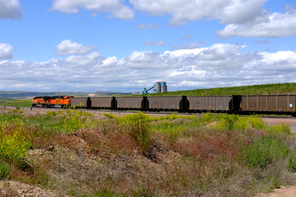BNSF diesel locomotives 6061 and 9941 and TX UX marked freight cars moving to be loaded with coal along a spur line with coal silos in the background at Eagle Butte Mine in Campbell County, Wyoming