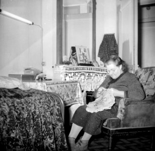 Bordurende vrouw gezeten in een fauteuil in haar woonkamer, Bestanddeelnr 252-9339