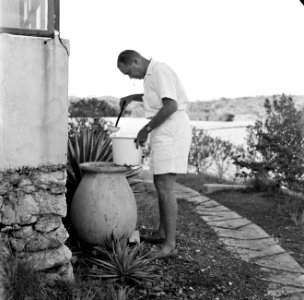 Bill schept regenwater uit een pot bij een huis aan de Fuikbaai, Bestanddeelnr 252-3035