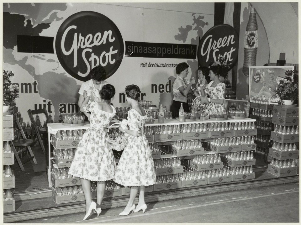 Bloemenmeisjes bij de stand van de Amerikaanse frisdrankfabrikant Green Spot op de Haarlemse voorjaarsbeurs in het Krelagehuis. NL-HlmNHA 54010545