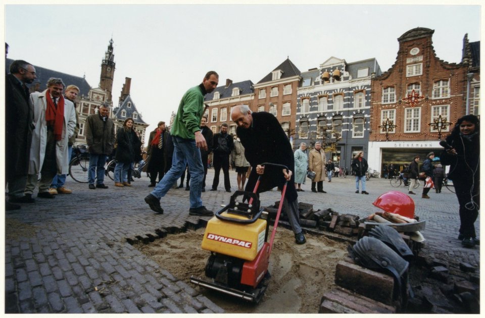 Burgemeester Pop is druk in de weer met een trilplaat. hij gaf hiermee het startsein voor de herbestrating van de Grote Markt. NL-HlmNHA 54037062