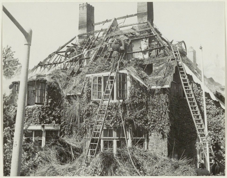 Brandweerman bij het nablussen van een villa met rieten kap. NL-HlmNHA 54011224