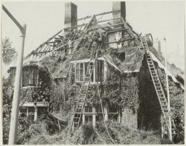 Brandweerman bij het nablussen van een villa met rieten kap. NL-HlmNHA 54011224