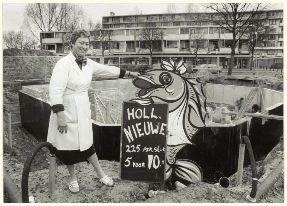 Bouw van het winkelcentrum Delftwijk. Foto Visverkoopster mevrouw De Haan voor de bouwput. NL-HlmNHA 54031837
