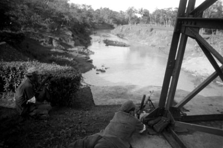 Brenschutter in positie bij een brug over een rivier, links van hem een soldaat, Bestanddeelnr 2561