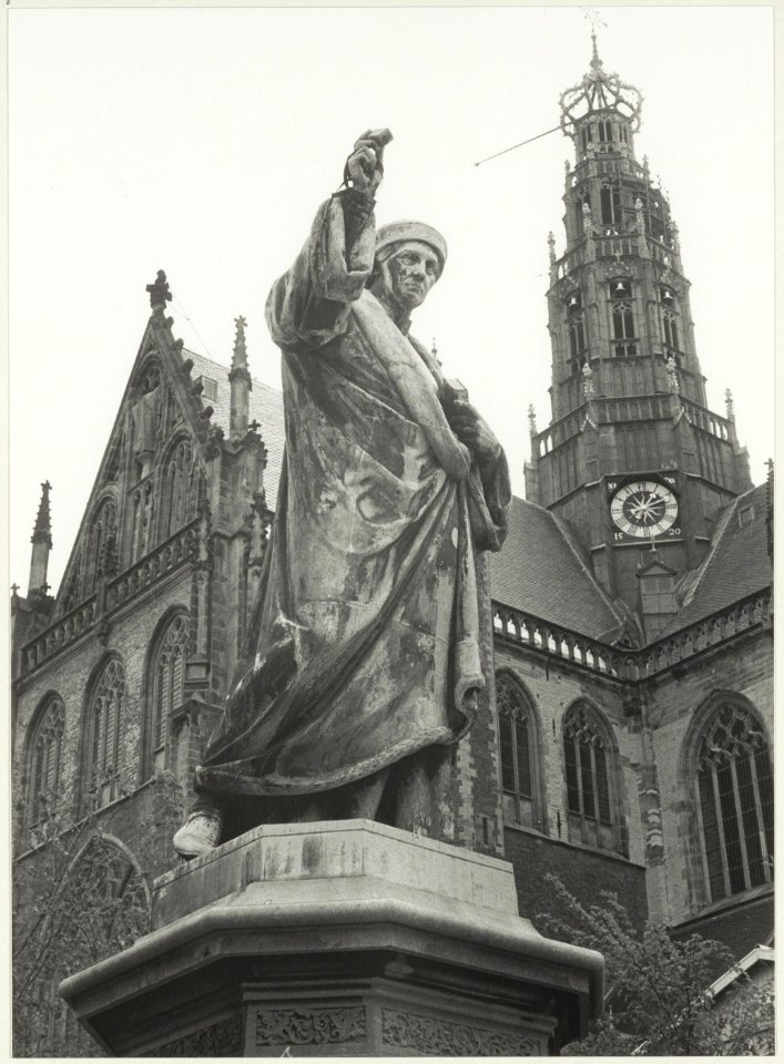 Close-up van het standbeeld van Lourens Jansz. Coster met de Grote Kerk als achtergrond. NL-HlmNHA 54021230