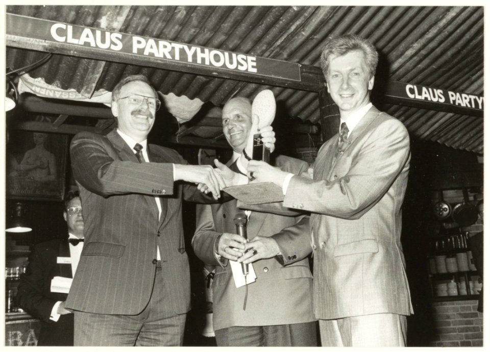 Claus Partyhouse Ondernemer van het jaar Jan Prins(l) ontvangt de keitrofee uit handen van de voorzitter van het KNOV J. Kamminga. In het midden Barry Hughes. NL-HlmNHA 1478 5650
