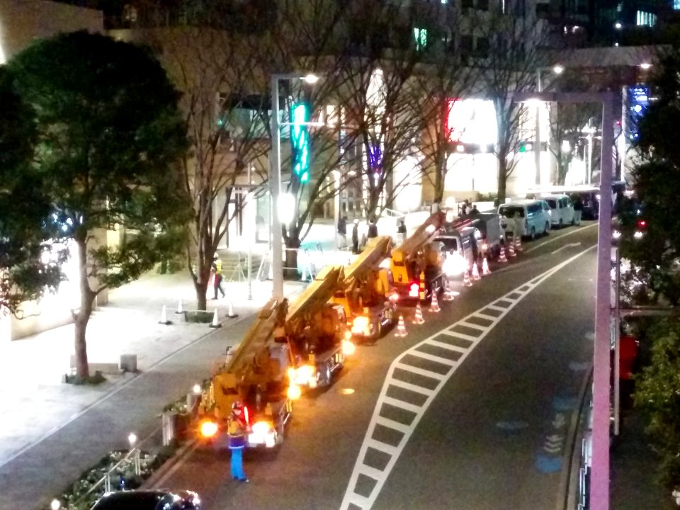 Crane trucks abfut to remove Christmas illuminations from trees, in Keyakizaka