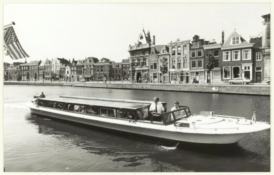 De speciale platte rondvaartboot van rederij Haarlem vaart over het Spaarne langs het Teylers Museum, NL-HlmNHA 54031443