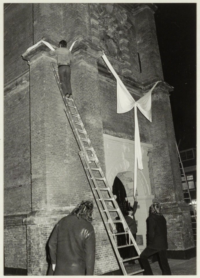 De toren van de Nieuwe Kerk wordt na de restauratie onthuld. De roze strik die door buurtbewoners om de toren was geknoopt, werd door gemeenteambtenaren van monumentenzorg niet echt op prijs, NL-HlmNHA 54011445