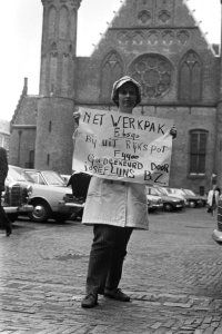 Demonstrante op het Binnenhof met een bord met de tekst Net werkpak F. 6590. B, Bestanddeelnr 924-5861