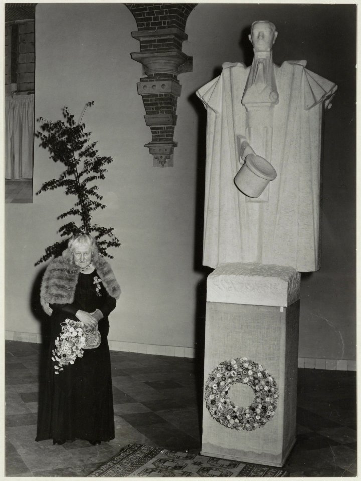 De 81 jarige dochter van Nicolaas Beets opent de tentoonstelling De Camera Obscura in de Vleeshal. Naast haar het beeld van Hildebrand door Bronner. NL-HlmNHA 54010745