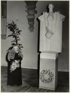 De 81 jarige dochter van Nicolaas Beets opent de tentoonstelling De Camera Obscura in de Vleeshal. Naast haar het beeld van Hildebrand door Bronner. NL-HlmNHA 54010745