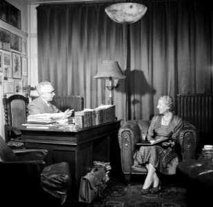 De heer Dellaert aan zijn bureau thuis. Met zijn echtgenote in een fauteuil, Bestanddeelnr 254-2442