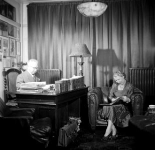 De heer Dellaert aan zijn bureau thuis. Met zijn echtgenote in een fauteuil, Bestanddeelnr 254-2441