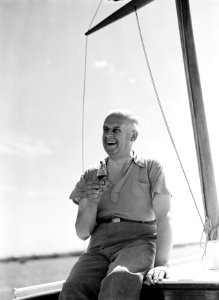 De heer Hagedoorn lachend met drankje, zittend op de kajuit van een zeilboot, Bestanddeelnr 252-1317