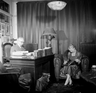 De heer Dellaert aan zijn bureau thuis. Met zijn echtgenote in een fauteuil, Bestanddeelnr 254-2440