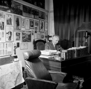 De heer Dellaert aan zijn bureau thuis. Met op de achtergrond foto's en karikatu, Bestanddeelnr 254-2435