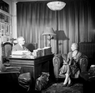 De heer Dellaert aan zijn bureau thuis. Met zijn echtgenote in een fauteuil, Bestanddeelnr 254-2443