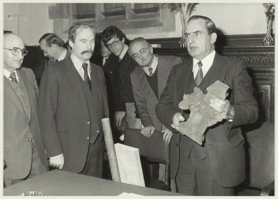 De heer Vermaire, president-kerkvoogd, overhandigt de kruisbloem aan aannemer Jurriëns met het verzoek het brokstuk zo spoedig mogelijk op de oorspronkelijke plek te bevestigen. Hiermee werd, NL-HlmNHA 54011550