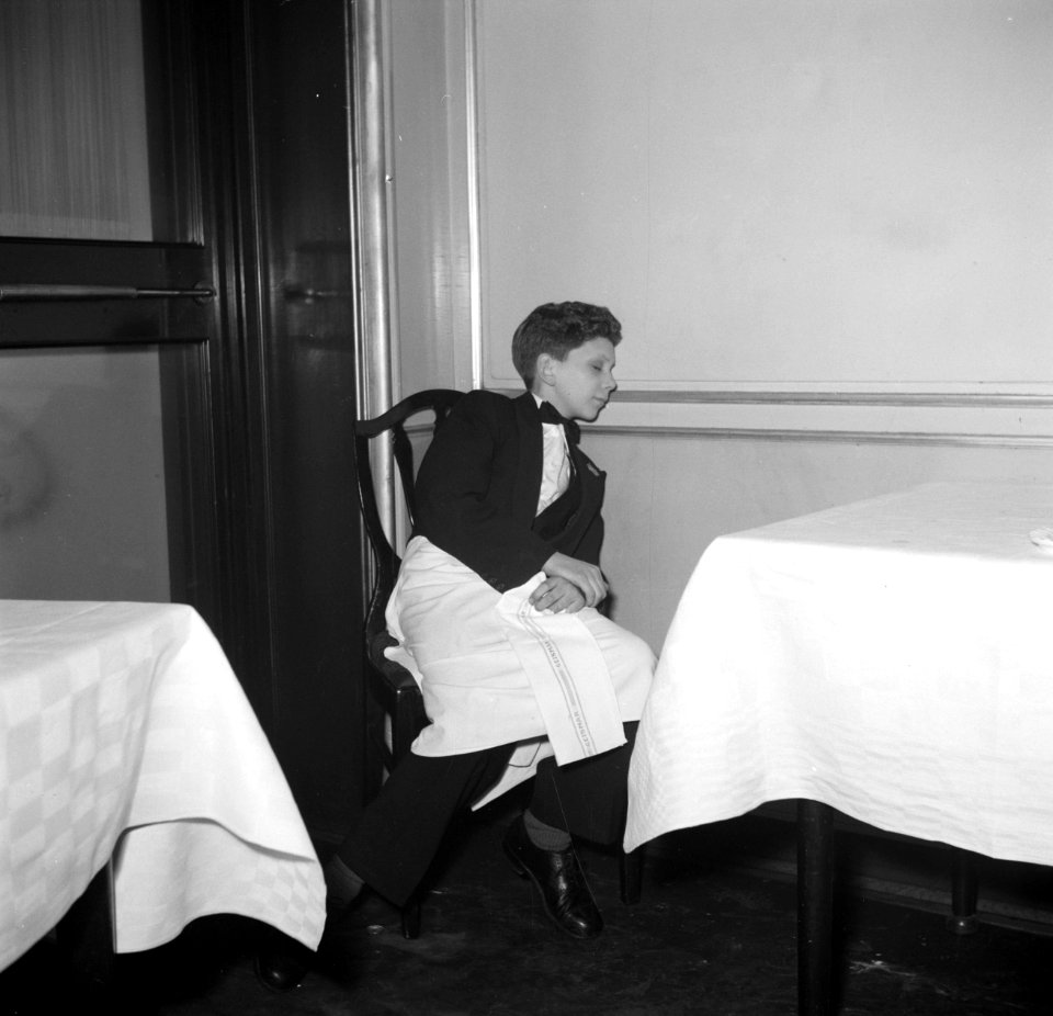 De kleinste en jongste ober slapend aan een tafel in restaurant Wivex, Bestanddeelnr 252-9190