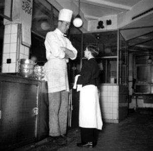De kleinste en jongste ober naast een kok in de keuken van restaurant Wivex, Bestanddeelnr 252-9183