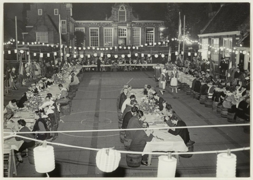 De deelnemers van het toneelspel De Vrijheid Vlagt aan de koffietafel voor de Stadsdoelen. NL-HlmNHA 54011127
