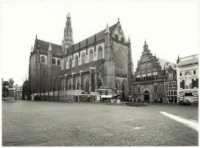 De Grote of St. Bavokerk, rechts van de kerk de Vleeshal. Voor de kerk het beeld De Zonnevechter. NL-HlmNHA 54037586