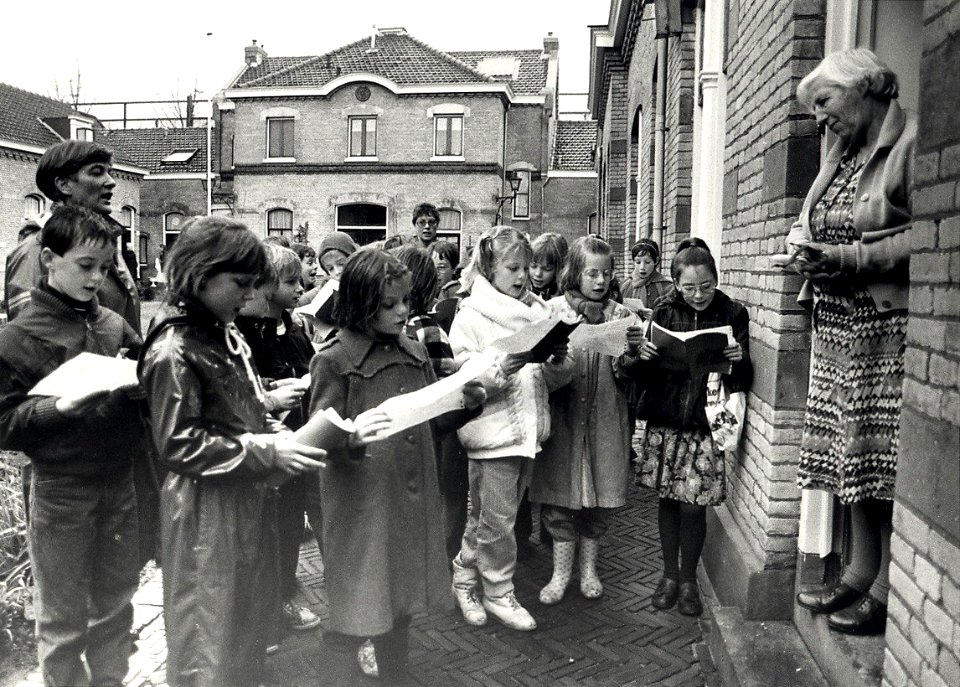 De derde klas van de Dreefschool zingt voor de bejaarde-bewoners van het Zuiderhofje aan de Zuiderstraat. Geschonken in 1989 door United Photos de Boer bv. - Gepubliceerd in het Haarlems Dagblad van 2