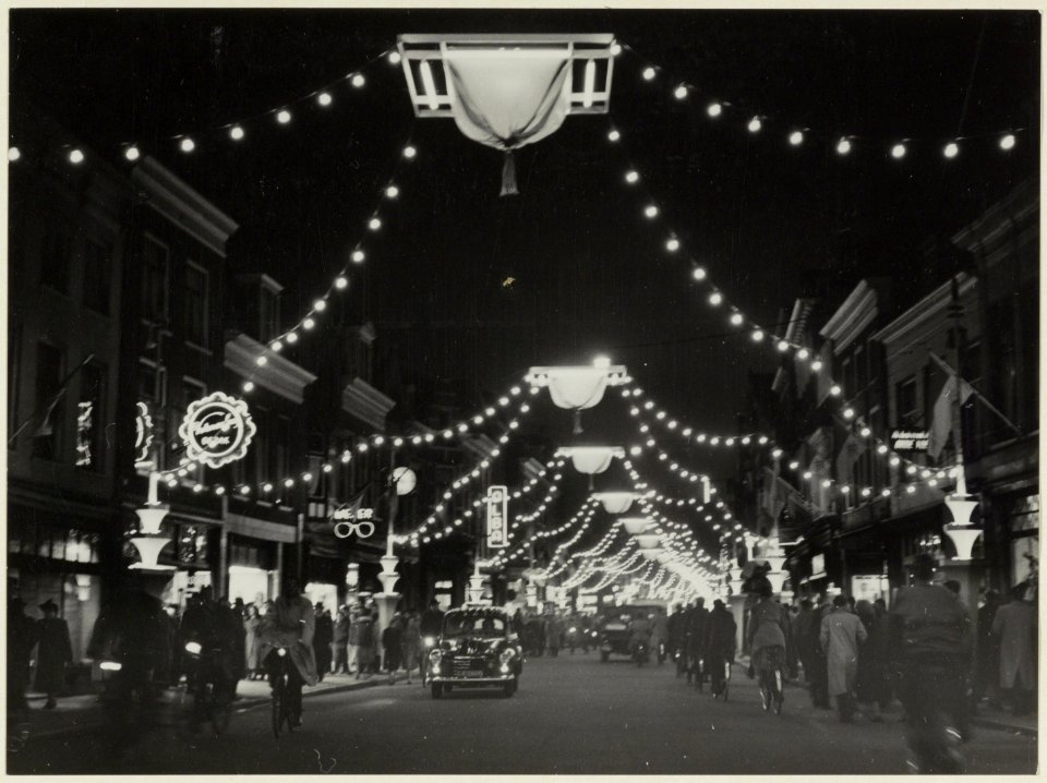 De Grote Houtstraat nabij de Grote Houtbrug, ziende naar het noorden, bij avond versierd en verlicht. NL-HlmNHA 54004649