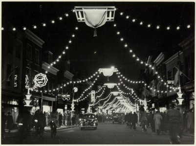 De Grote Houtstraat nabij de Grote Houtbrug, ziende naar het noorden, bij avond versierd en verlicht. NL-HlmNHA 54004649