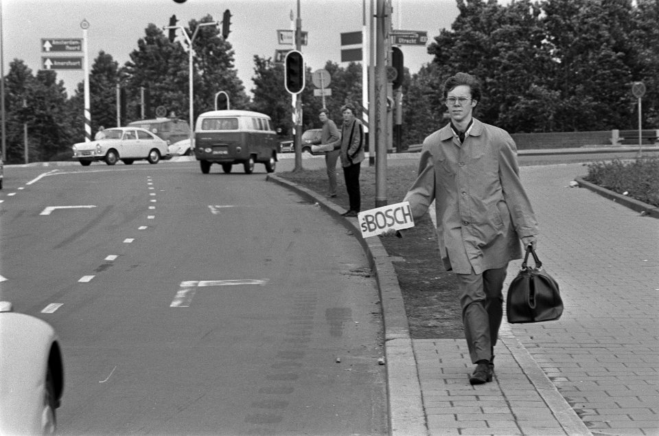 Drie jongens staan voor een stoplicht te liften, een met tas en bestemming Den …, Bestanddeelnr 923-6368