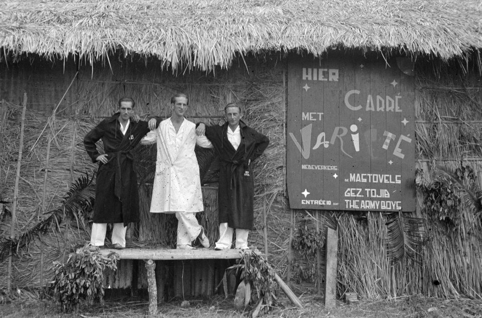 Drie mannen - acrobaten - poseren in badjassen voor een grote hut met het opsch, Bestanddeelnr 1653-5-1