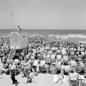 Drukbezocht strand met badgasten in strandstoelen, aan de linkerkant een strandw, Bestanddeelnr 255-1974