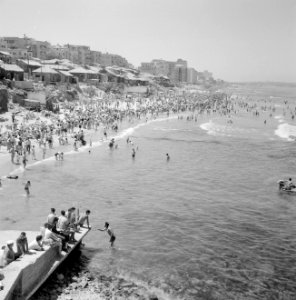 Druk bezocht strand waar badgasten in zee zwemmen (aan de kant zit een man met h, Bestanddeelnr 255-1947