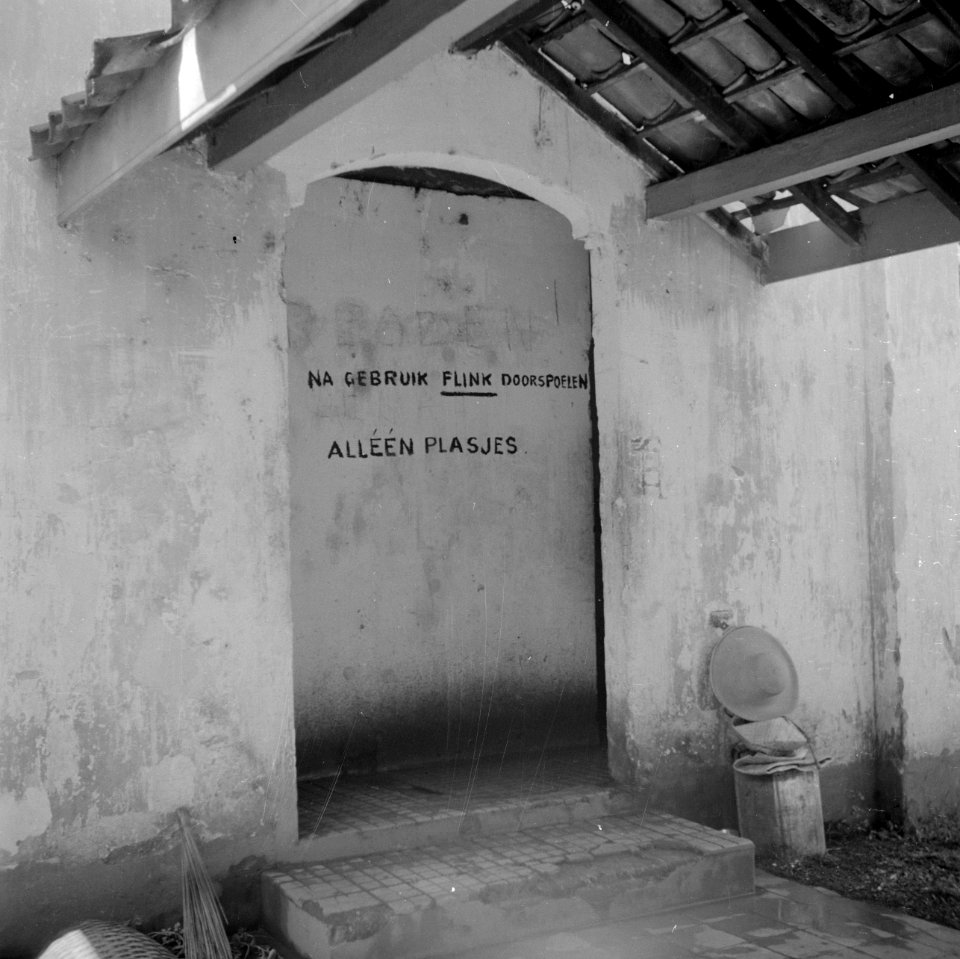 Deurgat in het Adek-kamp en een muur met het opschrift Na gebruik flink doorspo, Bestanddeelnr 255-8173