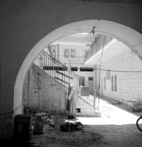 Doorkijkje door boog in muur naar een trap en de woonhuizen die aan een gallerij, Bestanddeelnr 255-2452