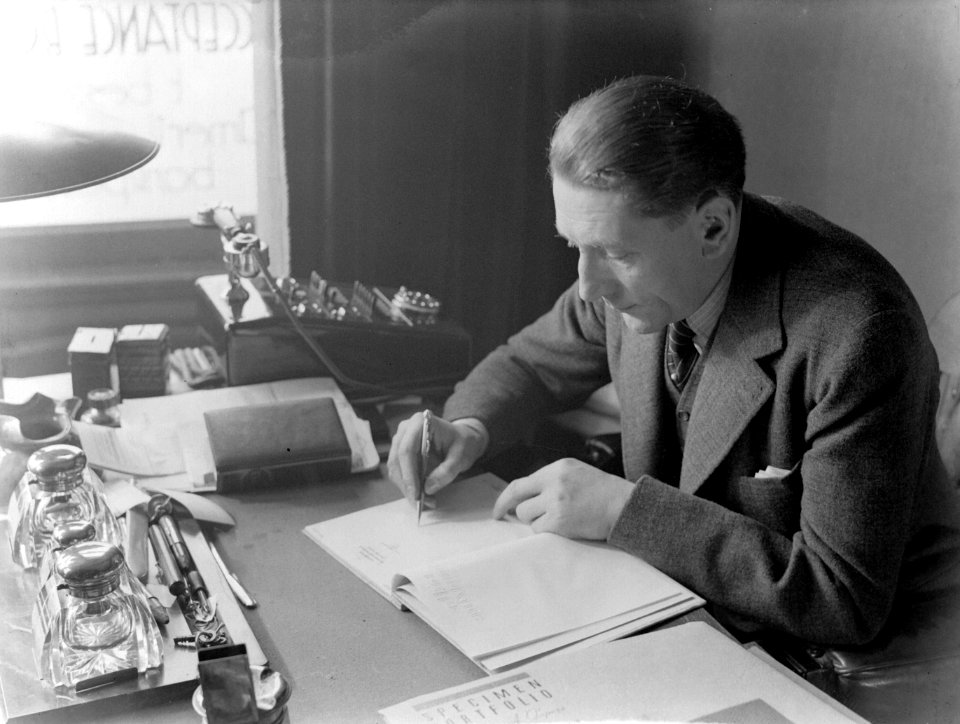 Eli de Vries zit aan zijn bureau met daarop een telefoon, een inktstel en docume, Bestanddeelnr 189-1157