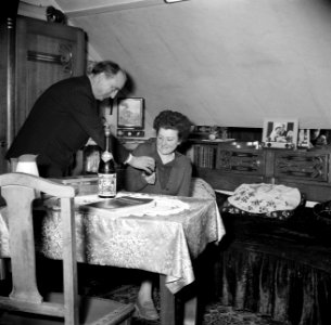 Echtpaar aan tafel in de woonkamer de man reikt zijn vrouw een glaasje aan, Bestanddeelnr 252-9337